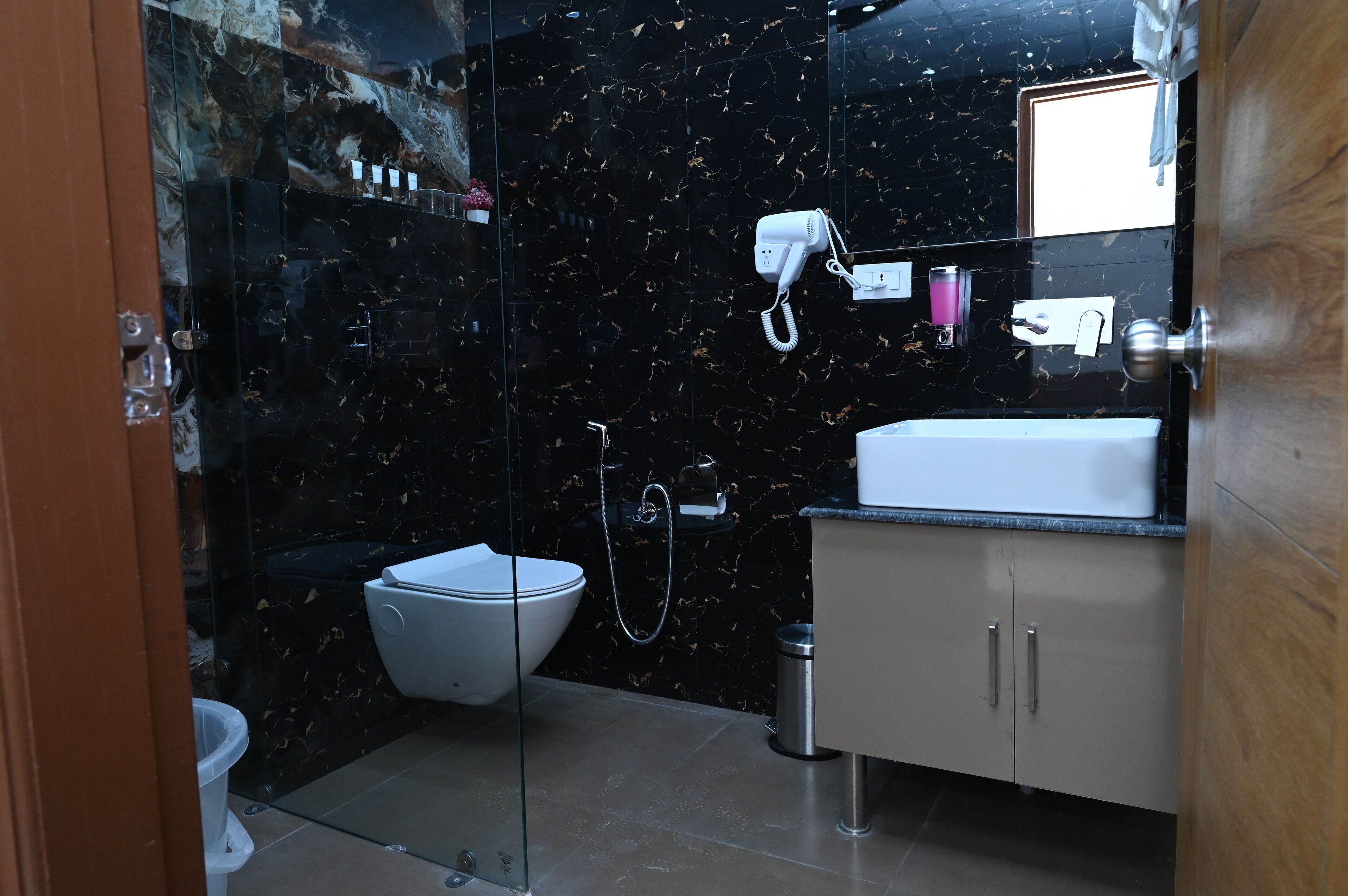 A modern bathroom with a black marble backsplash, a white toilet, a glass-enclosed shower, and a vanity with a sink and cabinet.