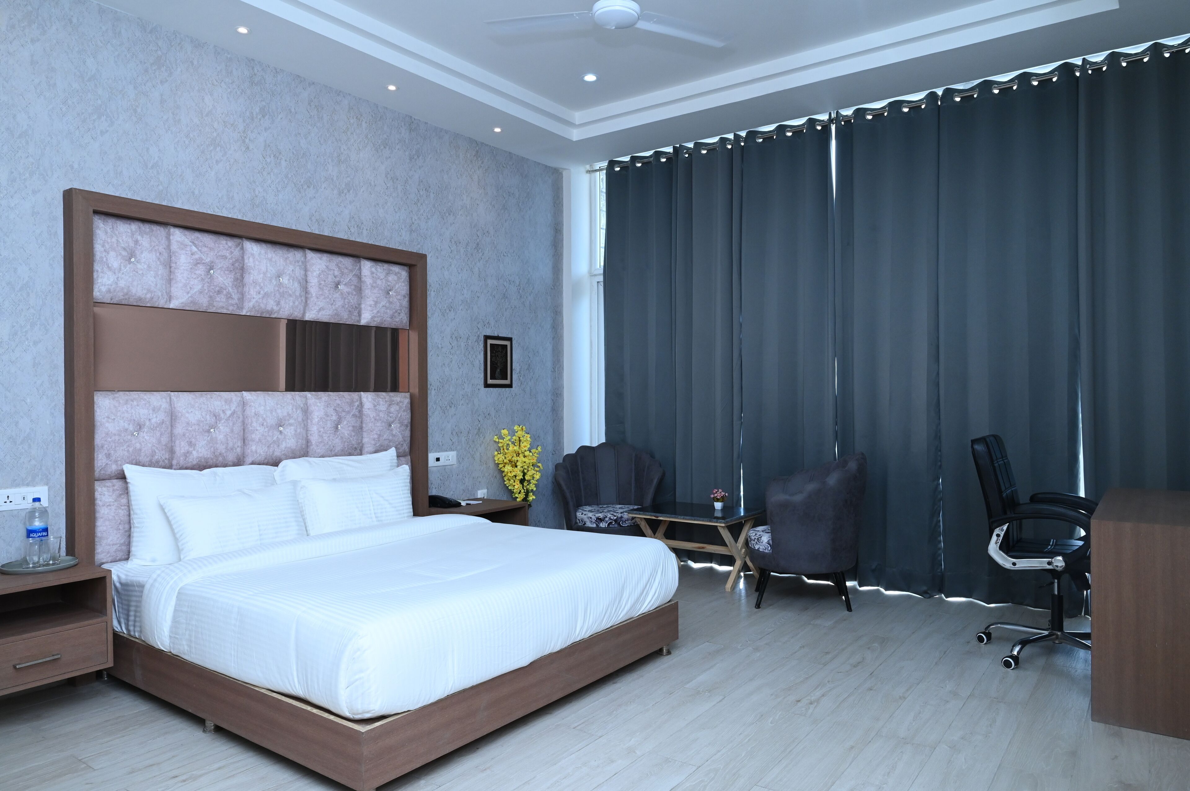 A hotel room with a large bed, a desk, two chairs, and a dark curtain.