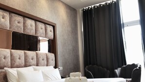 A modern hotel room with a large bed, a tufted headboard, a dark curtain, and a seating area with chairs. - SPT Clarks Inn Suite Mandi  (Balichauki)