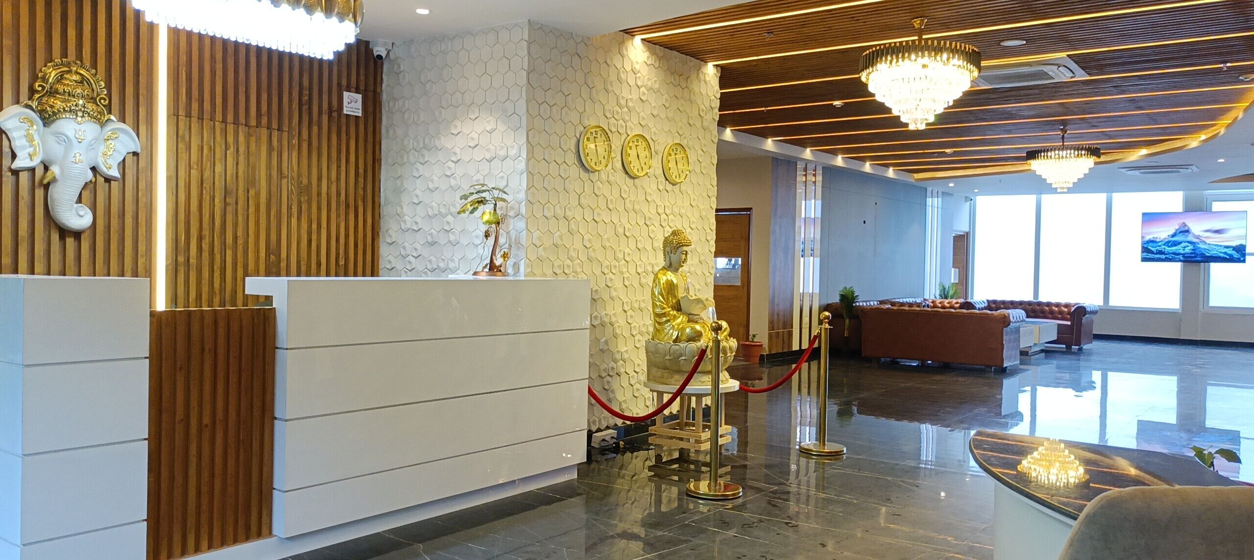 A hotel reception area with a wooden reception desk, a statue of an elephant, a Buddha statue, and a chandelier.
