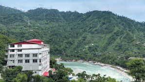 A multi-story building with a red roof, situated in a lush green valley with a river. - SPT Clarks Inn Suite Mandi  (Balichauki)
