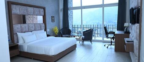 A modern hotel room with a large bed, a desk, a chair, and a TV.
