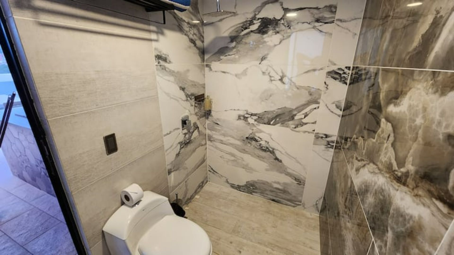 A bathroom with a toilet, marble walls, and a shower area.