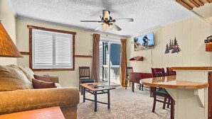 Un salon confortable avec un canapé, une table basse et une table à manger. Un ventilateur de plafond et un téléviseur sont fixés au mur.