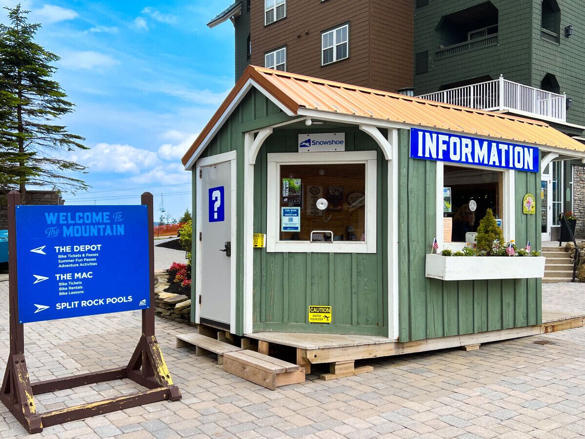 Een klein informatiepunt in de bergen, met een groene buitenkant en een blauw bord waarop 'INFORMATION' staat.