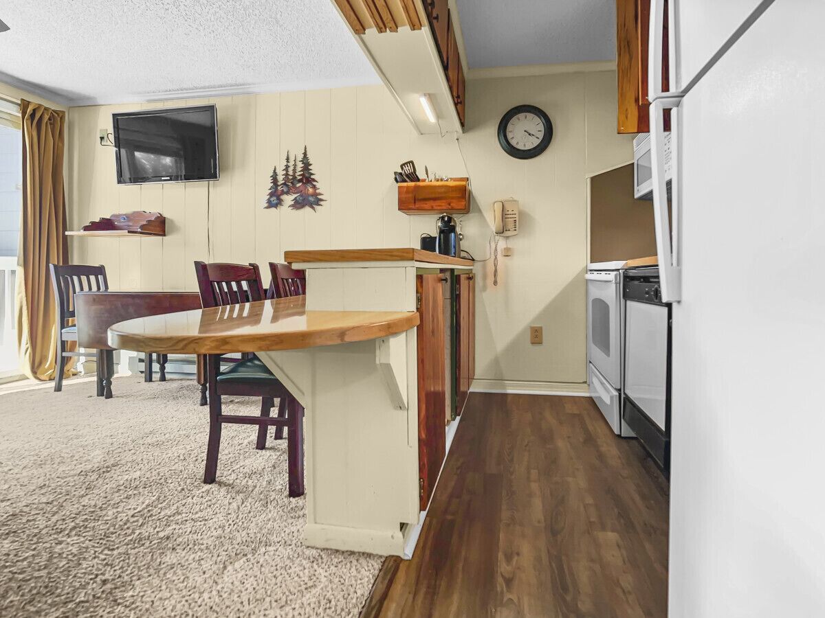A compact living space with a dining area, kitchenette, and a TV mounted on the wall.