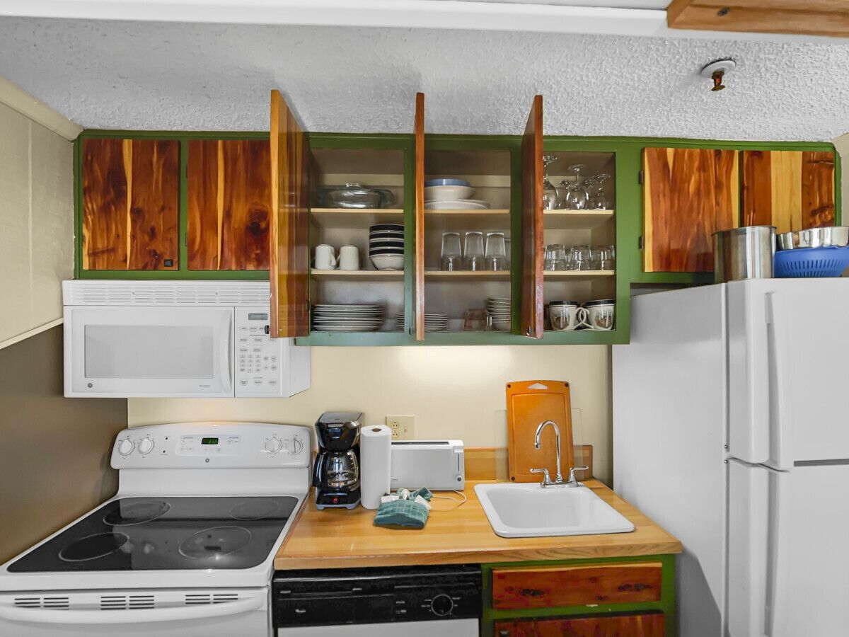 Une cuisine de taille réduite équipée d’un four à micro-ondes, d’une cuisinière, d’un évier et d’armoires en bois.