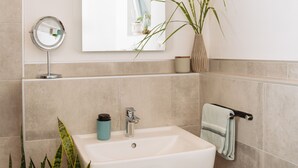 A bathroom with a white sink, a mirror, a towel rack, a potted plant, and a framed picture on the wall.