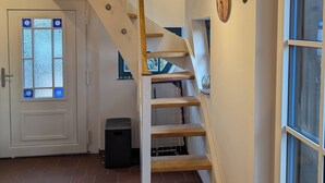 Un escalier avec des marches en bois et une rampe blanche, menant à un palier doté d’une porte et d’une fenêtre à vitres dépolies.