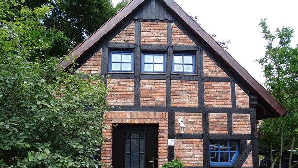 Une maison à deux étages avec une porte noire, un petit porche et une façade en briques.