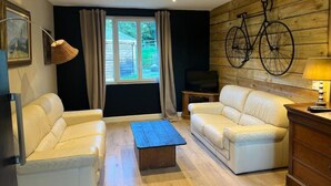 A living room with two cream sofas, a wooden coffee table, a television on a wooden stand, and a wall-mounted bicycle decoration. - Chez Caroline Ingalls (Gavray-sur-Sienne)