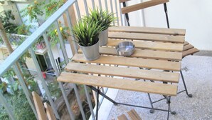 Een houten tafel en stoelen op een balkon, met een bloempot en een metalen kom.