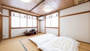 A traditional Japanese room with tatami flooring, a bed with white bedding, a small wooden table, and sliding shoji doors.