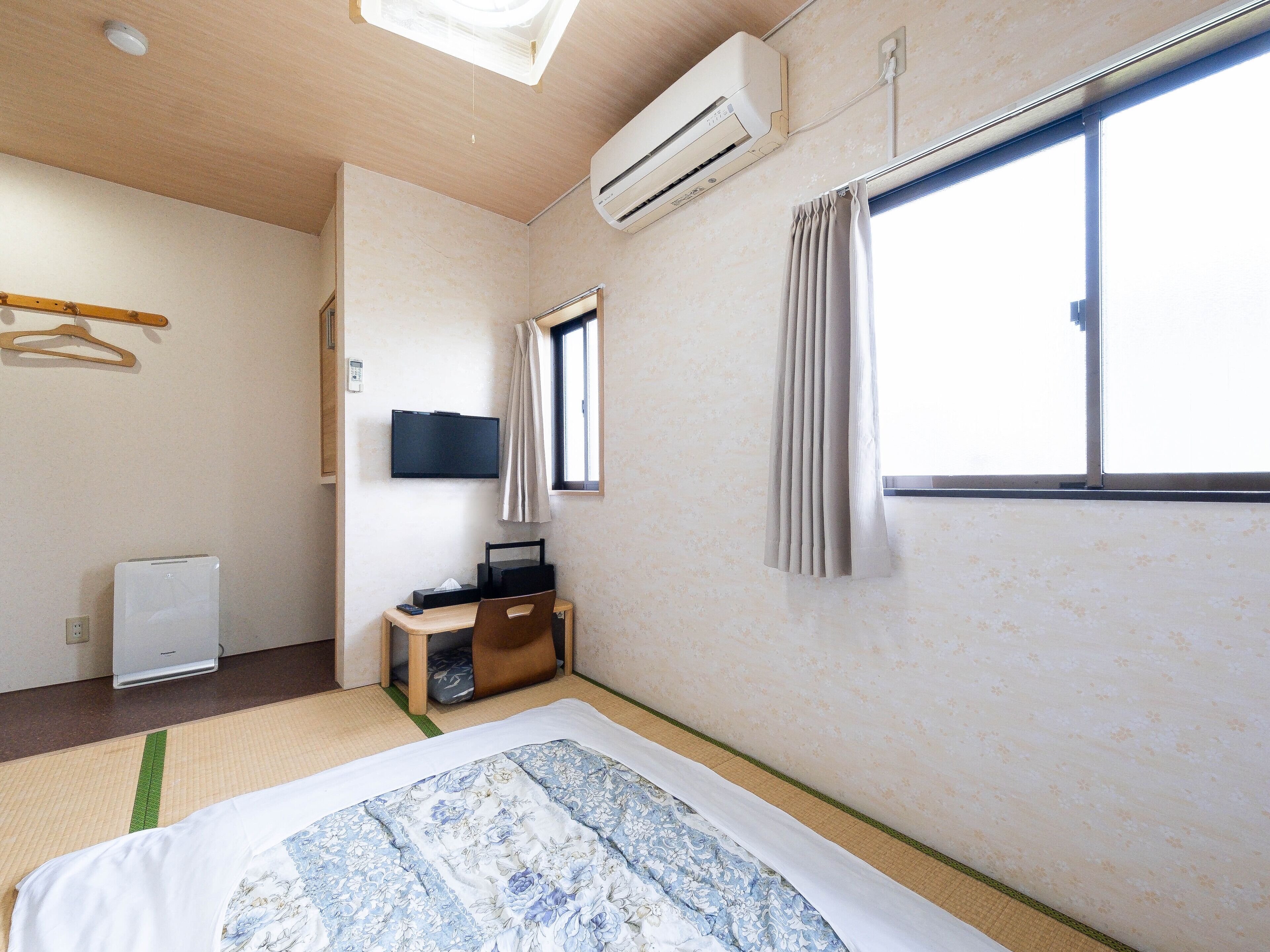Quarto de hotel com cama, escrivaninha, televisão, ar condicionado e janela com cortinas.