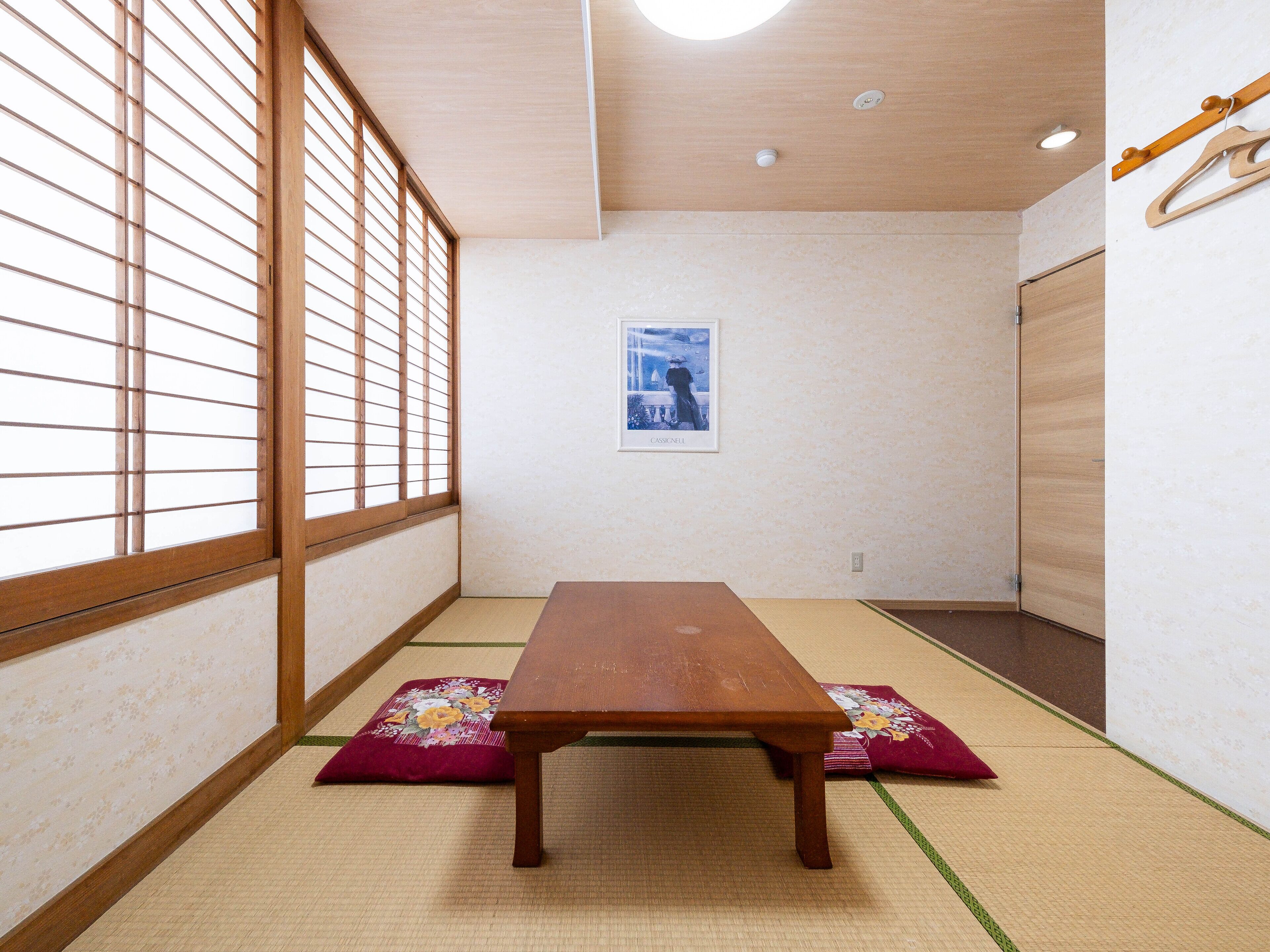 A traditional Japanese room with tatami flooring, a low wooden table, shoji screens, and a framed picture on the wall.