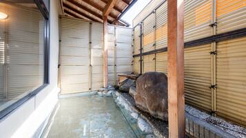 Experience a serene onsen bath area with a rustic atmosphere, featuring a stone basin and natural light filtering through shoji screens.