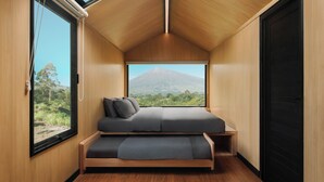 Une petite pièce comprenant un lit, une fenêtre et donnant sur une montagne.
