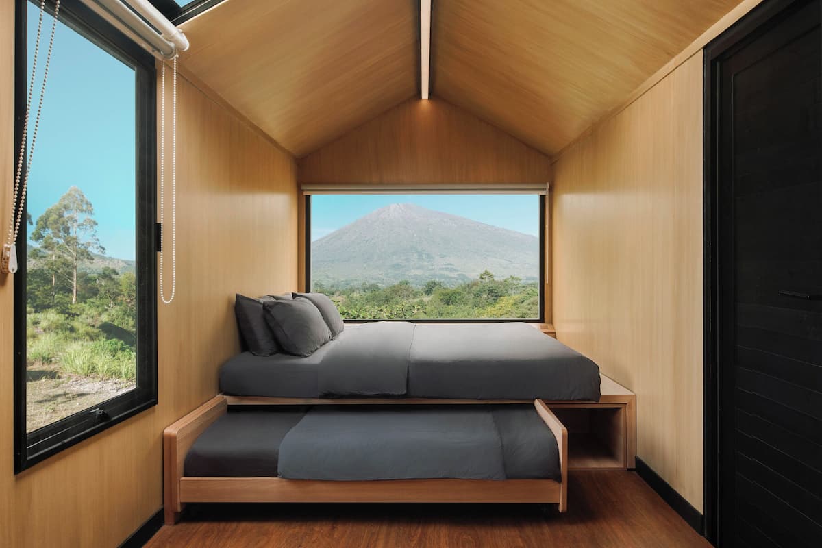 Een kleine kamer met een bed, een raam en uitzicht op een berg.