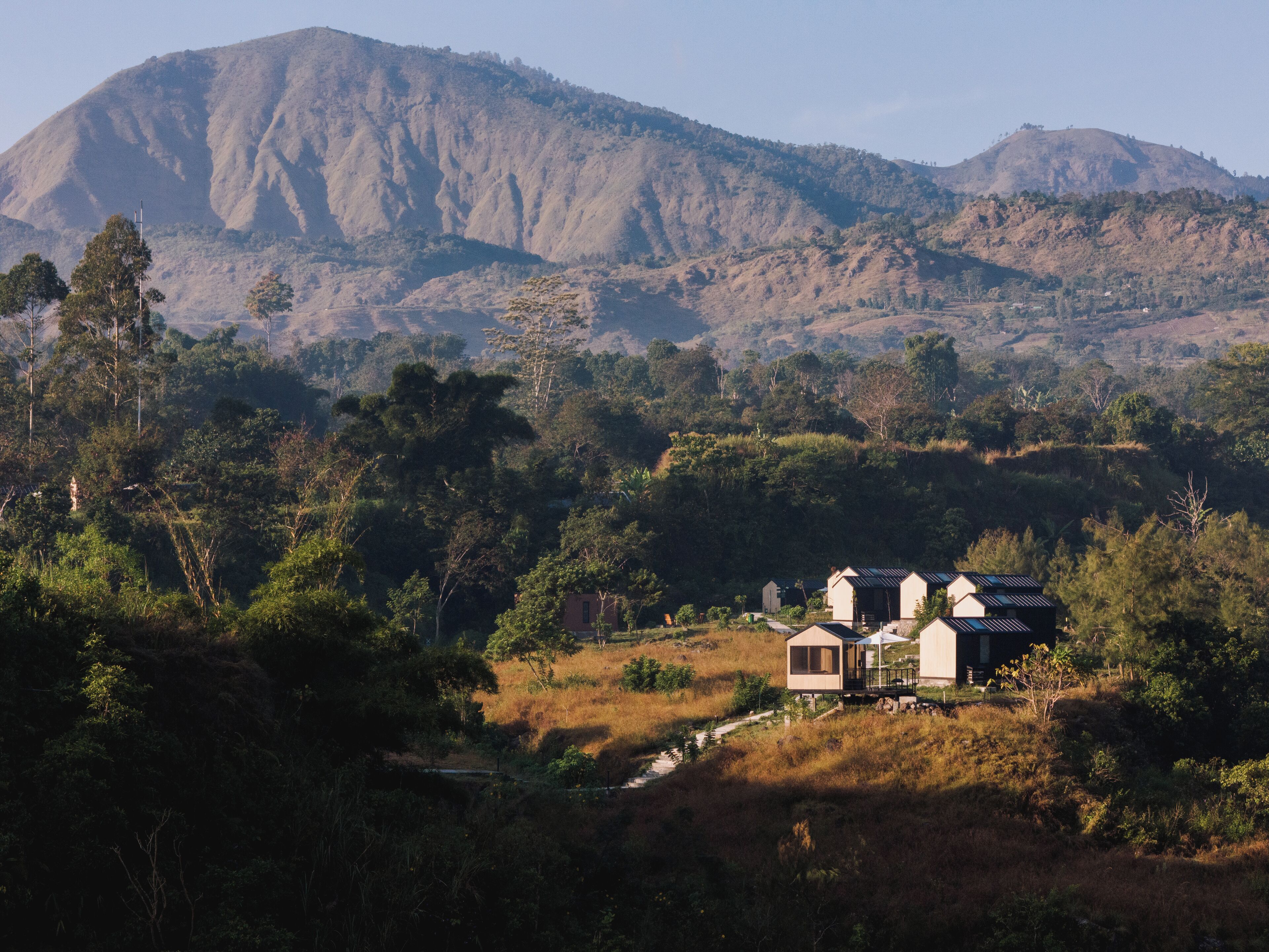 A rural setting with a house surrounded by dense vegetation and hills.