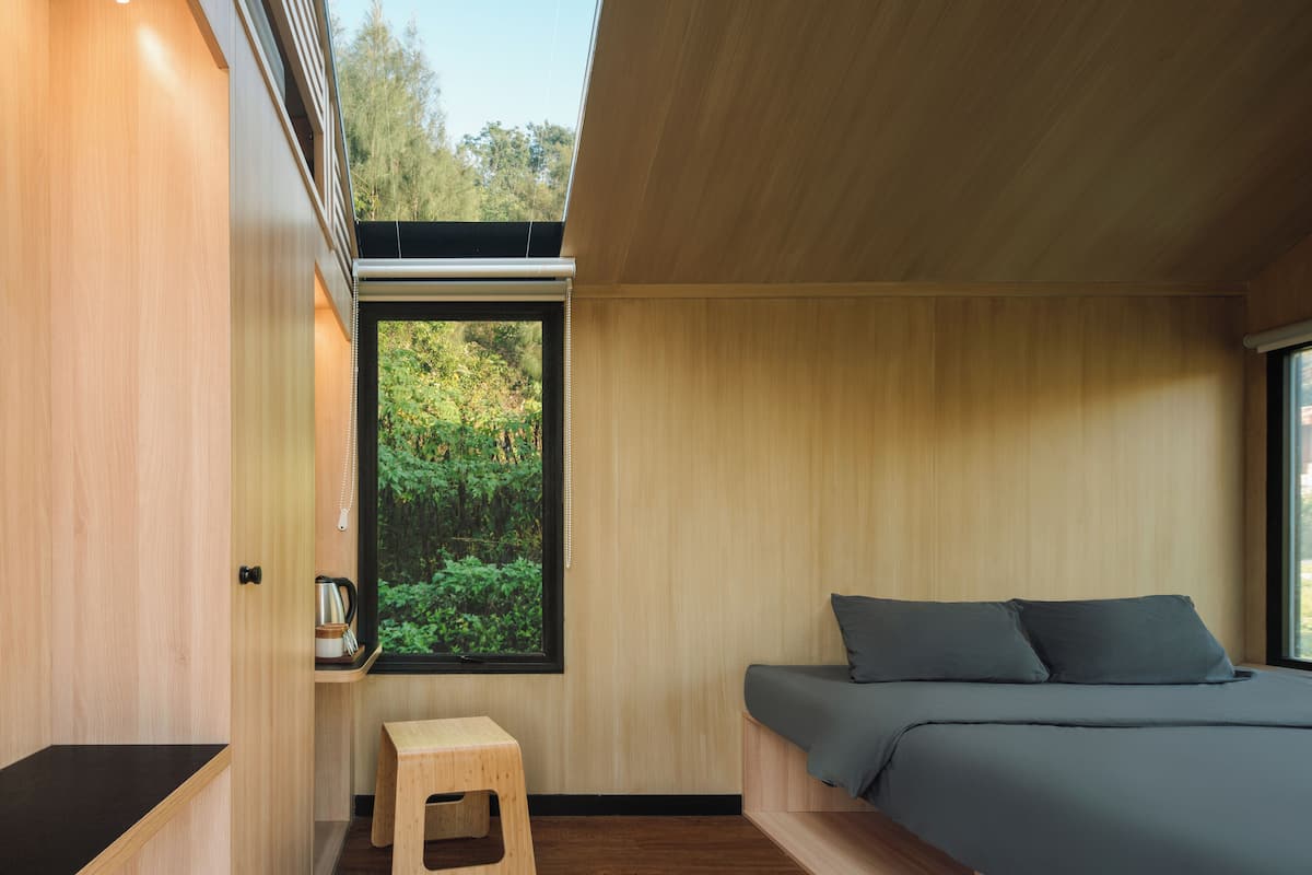 Een moderne slaapkamer met dakraam, een klein houten krukje en een bed met grijze beddengoed.