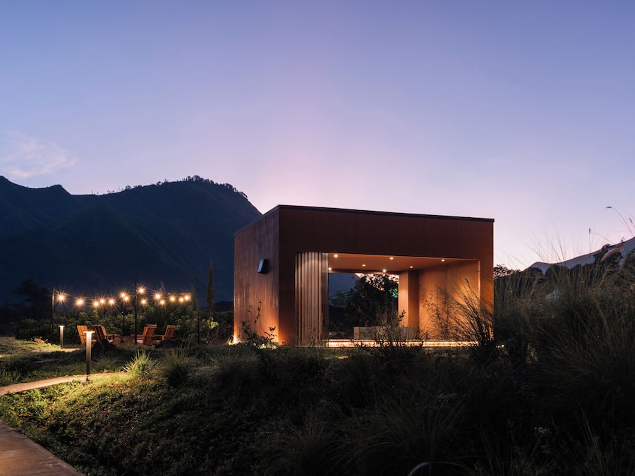 A modern building with an open design, surrounded by natural landscape and illuminated by ambient lighting.
