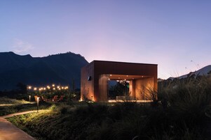 A modern building with an open design, surrounded by natural landscape and illuminated by ambient lighting.