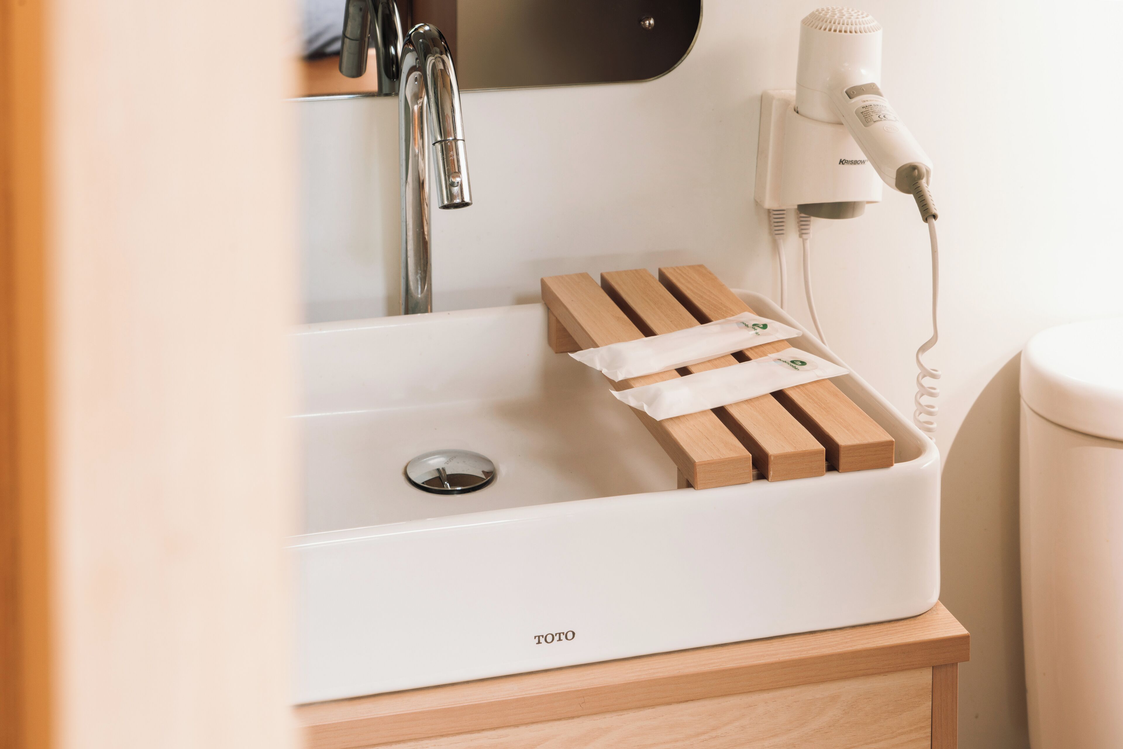 A bathroom with a white sink, a mirror, a hairdryer, and a wooden soap dish.