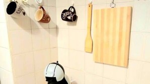 A kitchen with a coffee maker, a hanging wooden spoon, and a hanging mug with a coffee-related design. - Fionia In Gazi- Athens Center Apartment Num3585 (Athens)