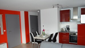 A modern kitchen with red cabinets, a dining area with a grey sofa, and a tiled floor. - Charming Gîte with Garden and Child's Play Area - Near Altkirch Center (Altkirch)