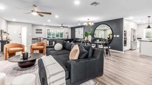 A modern living room with a sectional sofa, two armchairs, a coffee table, and a dining area with a round table and chairs. - The Monterey | Pool, Sport Court & Putting Green (Scottsdale)