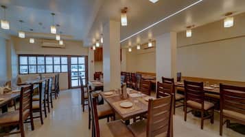 A spacious restaurant with multiple dining tables and chairs, large windows, and modern pendant lighting.