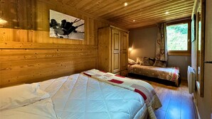 Ein Schlafzimmer in einer Holzhütte mit zwei Betten, einer Holzbalkendecke und einem Fenster mit Blick auf Grünflächen.