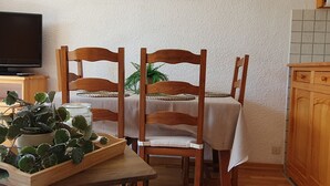 Ein Essbereich mit Tisch für zwei Personen, Holzkästen, einem Blumentopf und einem Fernseher auf einem Schrank.
