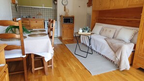 Ein gemütliches Zimmer mit einem Holzespeisetisch, Stühlen, einer Couch, einem kleinen Holzschrank und einer Küchenzeile mit Mikrowelle und Schränken.