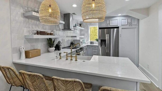 Une cuisine moderne dotée d’un grand îlot central, d’appareils électroménagers en acier inoxydable, de chaises en osier et de luminaires suspendus.