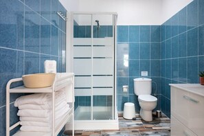 A bathroom with blue tiles, a glass shower enclosure, a toilet, and a sink.