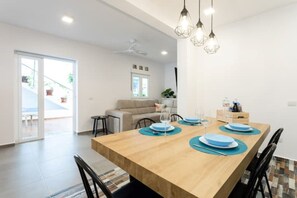 A modern dining area with a wooden table set for four, a sofa, and a ceiling fan.