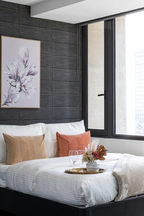 Un dormitorio moderno con cabecera de madera oscura, un ventanal grande y una obra de arte floral enmarcada.