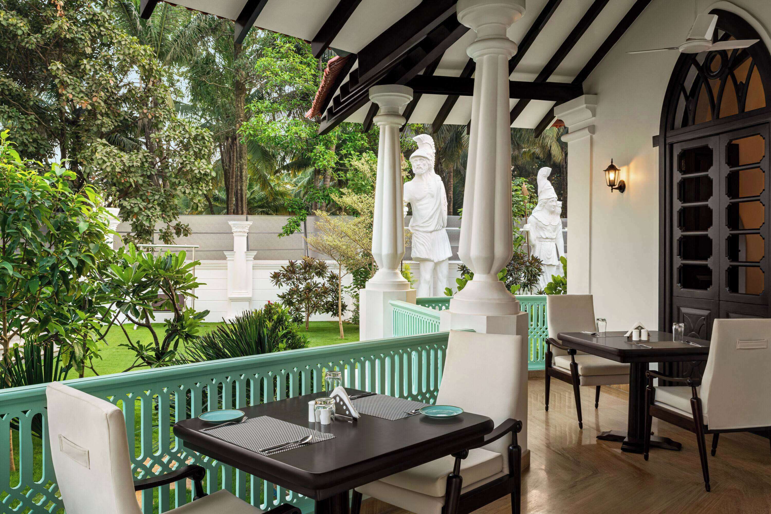 Un espace de restauration en plein air, avec une table et des chaises, entouré de verdure et de statues blanches.