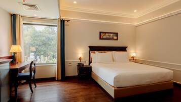 A hotel room with a large bed, a desk with a chair, a window with curtains, and a painting on the wall.