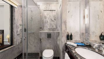 Een moderne badkamer met een douchecabine van glas, een marmeren wastafel en een toilet.