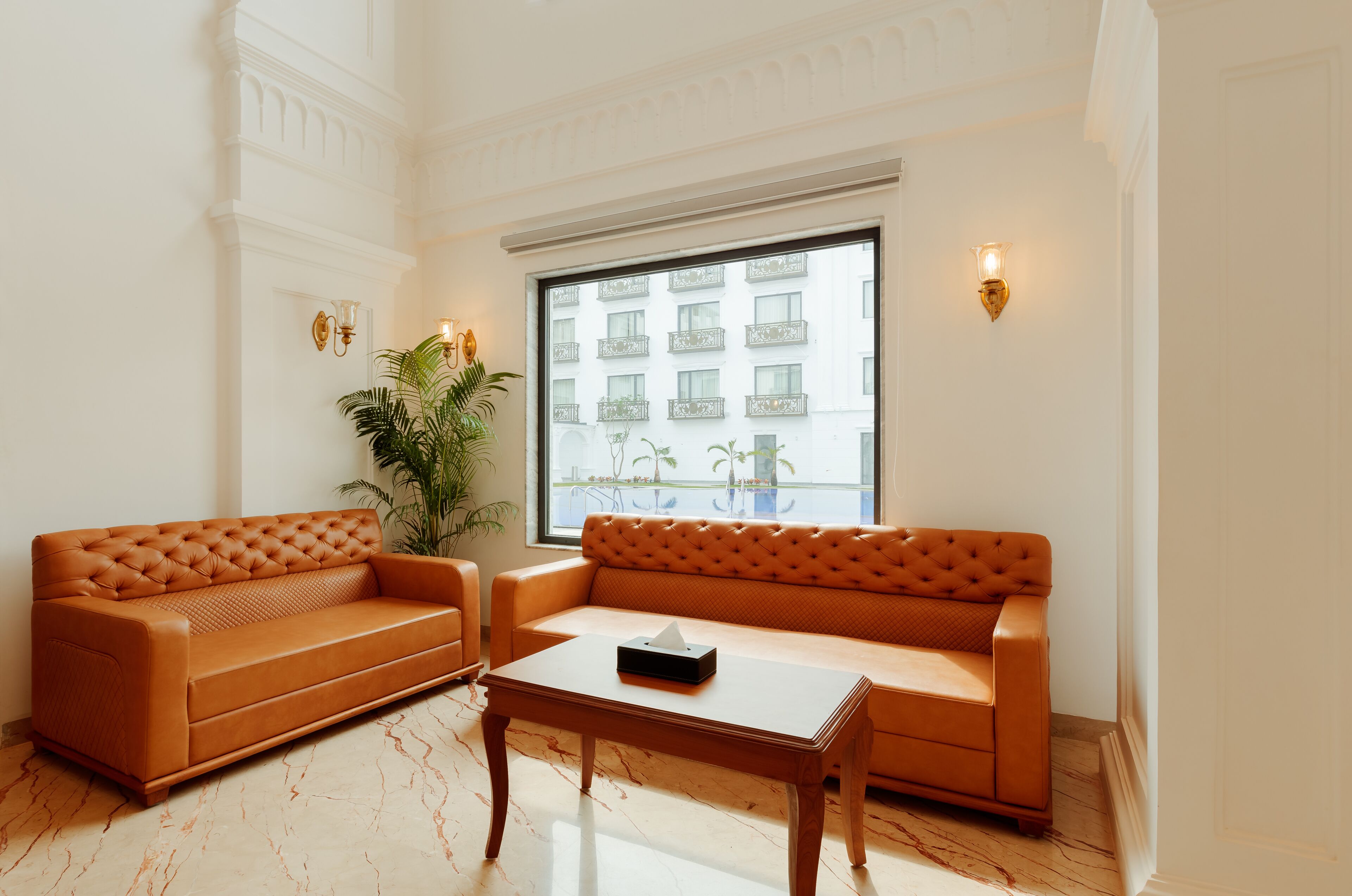 Een kamer met twee oranje banken, een houten salontafel en een groot raam met uitzicht op gebouwen.