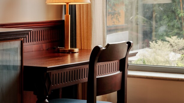 Ein Holztisch mit Lampe, Stuhl und einem Fenster mit Blick auf Grünflächen.