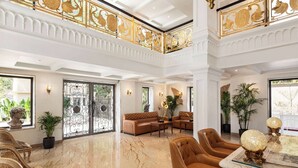 Een ruime lobby met een hoge plafond, marmeren vloeren en een statige trap met versierde balustrades.