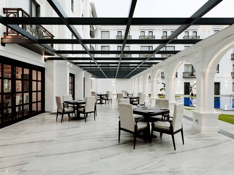 Un vaste espace extérieur aménagé pour les repas, avec plusieurs tables et chaises, une piscine et une allée couverte dotée de balcons.