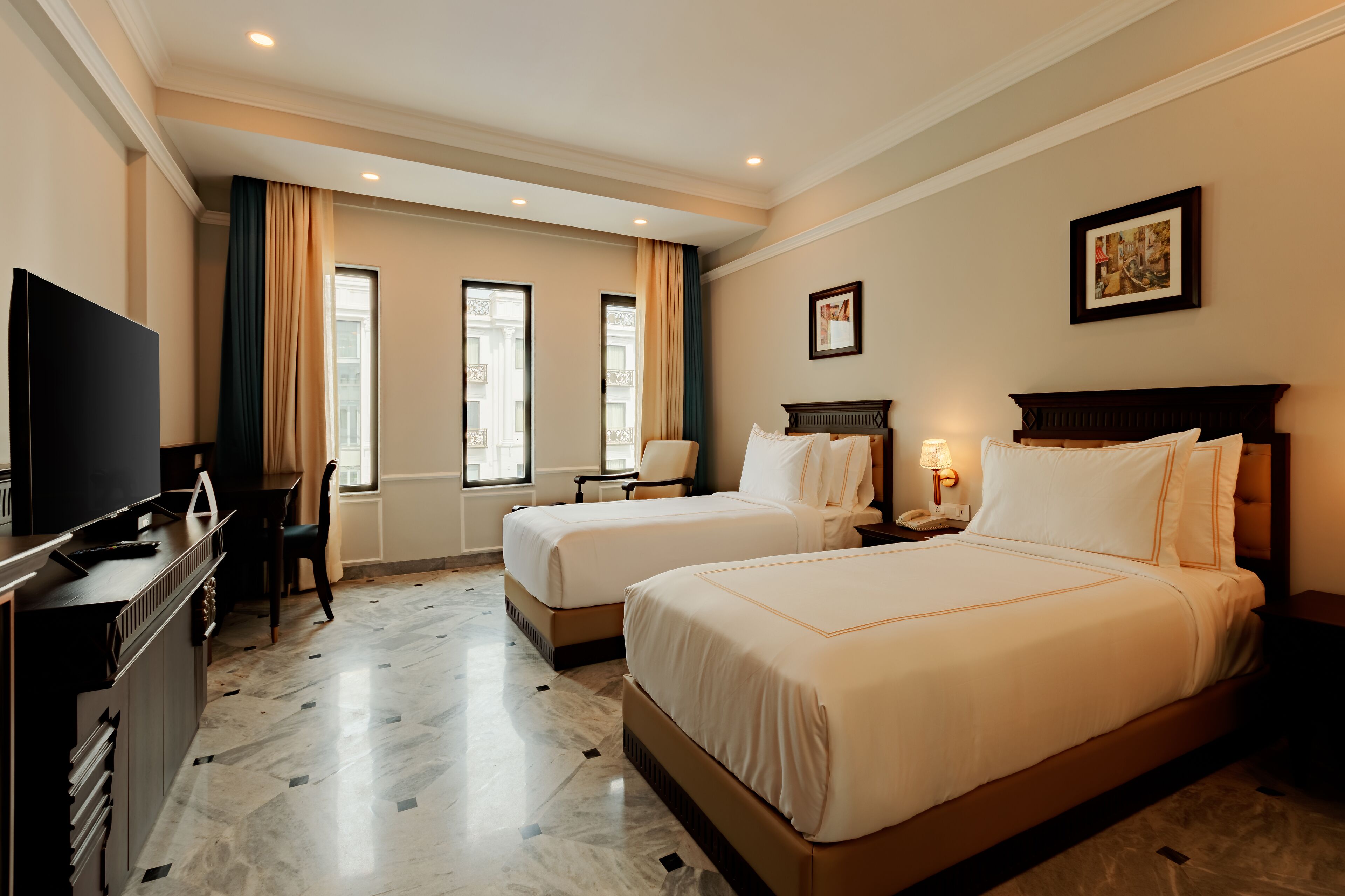 A hotel room with two beds, a desk with a TV, a chair, and a nightstand with a lamp.