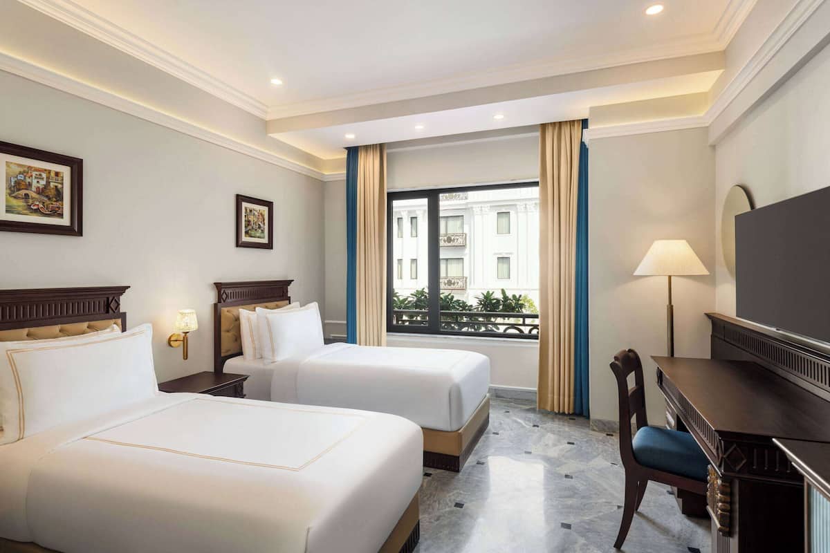 A hotel room with two beds, a desk, a chair, a TV, and a window with curtains.