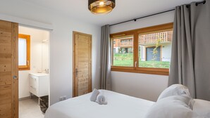 Une chambre à coucher avec un lit, une fenêtre donnant sur un immeuble et une porte en bois menant à la salle de bain.