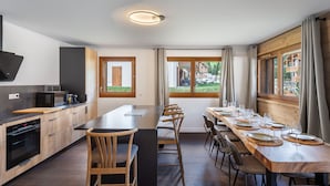 Une cuisine moderne avec des meubles en bois, un four à micro-ondes encastré et une grande table à manger pouvant accueillir six personnes, avec des chaises.