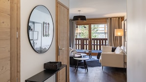 Une chambre d’hôtel avec un plancher en bois, un miroir rond, une petite table, un canapé et un balcon donnant sur un paysage verdoyant.